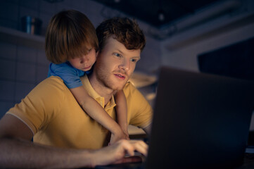 Ginger man nad his cute son watching something on internet in the evening
