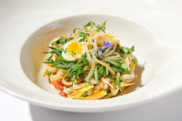 Healthy salad with squid and avocado on white plate with harsh shadows. Calamari salad with vegetables and eggs on white background with shadows of leaves. Summer food menu.