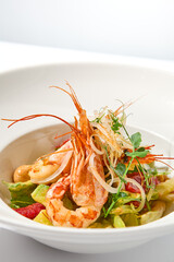 Elegant food - salad with shrimp and avocado on white table with harsh shadow. Flashy food concept. Seafood salad with shrimp, tomatoes and avocado on white plate with sunlight.