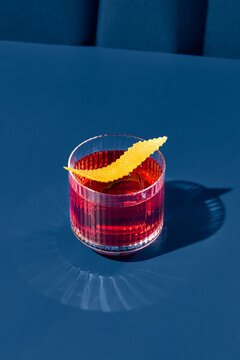 Popular cocktail negroni with gin and vermouth on blue background with shadow. Negroni cocktail on coloured background in trendy style. Contemporary concept with alcohol beverage. Bartender cocktail.