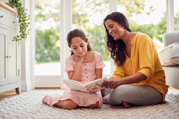 Mother And Daughter At Home Sitting On Floor In Lounge Reading Book Together
