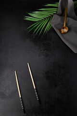 Fototapeta na wymiar Dark food background with textile, palm leaves and chopsticks. Black concrete background with empty place. Asian food menu. Black background with food ingredients for asian cuisine.