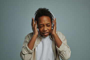 Cute boy of generation Alpha touching headphones on his head while keeping eyes closed and enjoying his favorite music