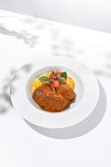 Traditional italian dish - osso buco with risotto milanese. Stew meat on bone with rice on white plate. Summer italian dining. Italian osso buco with garnish with hard shadows
