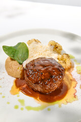 Beef cutlet with grilled cauliflower with gravy and cheese sauce on white plate. Elegant beefsteak on light background with shadows of sunlight. Summer menu with hard shadows Meat ball of minced meat