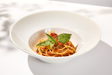 Vegetarian pasta with basil and tomatoes on white plate. Tomato pasta in summer menu with hard shadows Spaghetti with tomatoes on light background. Vegan food - spaghetti marinara