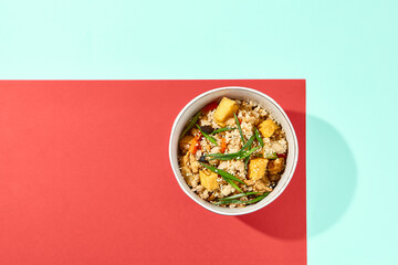 Fried rice with egg, chicken and vegetables on coloured background. Chinese food - fried rice with chicken in bowl on blue and red background. Nasi goreng with fried rice,chicken. Vibrant food.