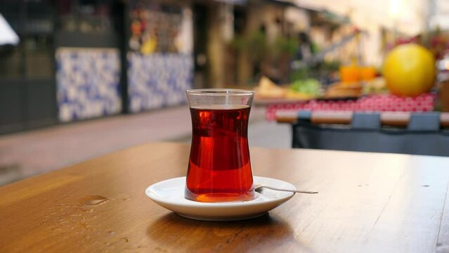 A Glass Full Of Hot Turkish Tea Is On Table At Cafe Sidewalk Terrace, Blurred Street On Background. White Vapor From Hot Drink Fly In Air. Breakfast Time At Morning Hour