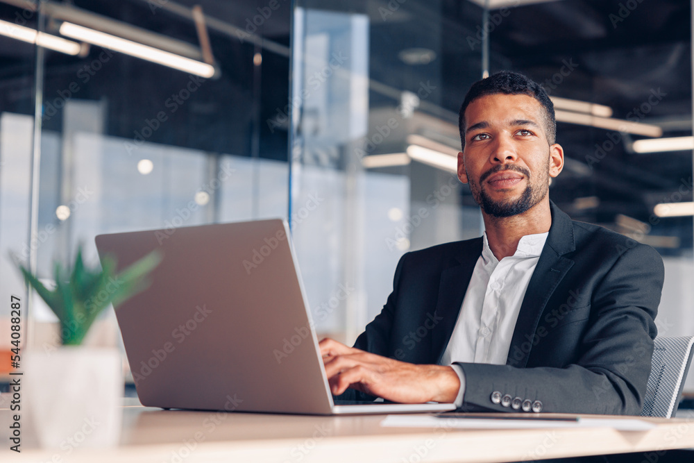 Canvas Prints handsome african businessman working laptop and looking away while sitting in modern office