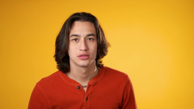 Portrait of Hispanic Latino gender fluid young hipster man 20s looks around put finger to lips shh quiet isolated on yellow background studio portrait
