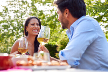 Couple Eating Outdoor Meal And Drinking Wine In Garden At Home Together