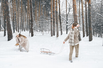 Fototapeta na wymiar Love romantic young couple girl,guy in snowy winter forest sledding,playing snowballs.Walking with sleigh in stylish clothes, fur coat,jacket, woolen shawl,bonnet.Snow lovestory.Romantic date,weekend