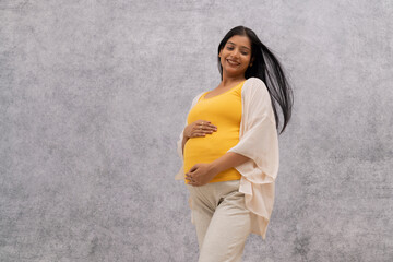 Happy pregnant woman standing against wall with holding her stomach