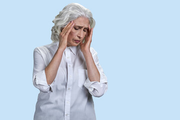 Senior woman suffering from severe headache. Isolated on blue.