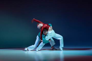 Fototapeta na wymiar Portrait of young couple, man and woman dancing, performing on stage isolated over dark blue background with mixed lights