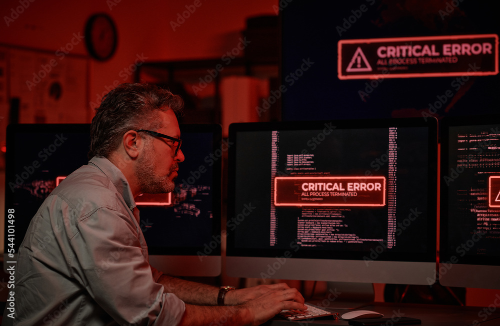 Poster Side view of serious mature IT support manager trying to solve technical problem while sitting in front of computer screens with critical errors on