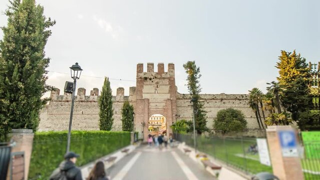 Road leads to Lazise Castle surrounded by lush greenery in Milan. Historical Italian landmark and tourists walking on sunny day hyper lapse