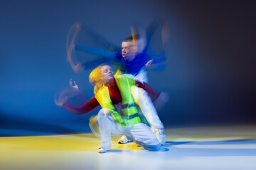 Portrait of young man and woman dancing isolated over blue yellow background with mixed lights....