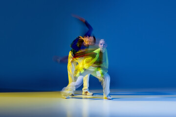 Fototapeta na wymiar Portrait of young man and woman dancing isolated over blue yellow background with mixed lights. Expression of freedom
