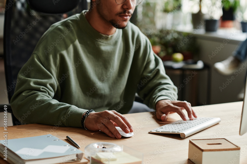 Poster Young man in casualwear clicking mouse and pressing key of computer keyboard while working over new software by workplace