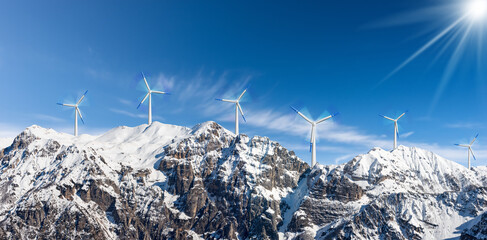 Group of white and blue wind turbines on the top of snow capped mountains against a clear blue sky...