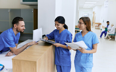 Medical employees. Medical assistant on duty talking with female nurses while working day in hospital standing near reception desk at lobby - 544105417