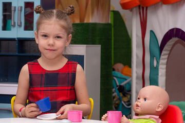 Portrait of happy and smiling caucasian little girl of 5 6 years old looking at camera sitting at doll table having tea time