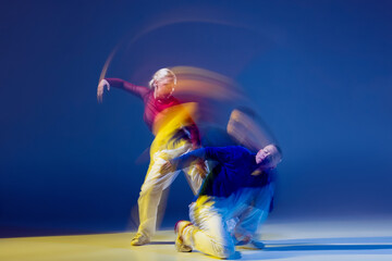 Portrait of young man and woman dancing breakdance isolated over dark blue background with mixed lights