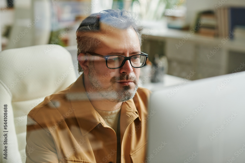 Poster Contemporary aged programmer or IT engineer working in front of computer and looking through information on screen