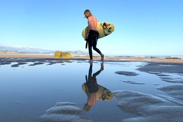 Surfer walking on the quiet beach with a surfboard under his arms