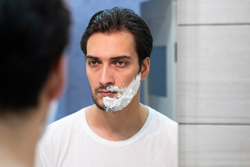 Handsome man looking at the mirror and shaving in the bathroom	