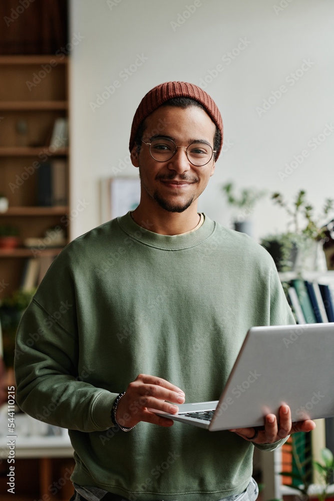 Poster Young confident IT engineer in casualwear looking at camera in office while using laptop and working with online or coded data