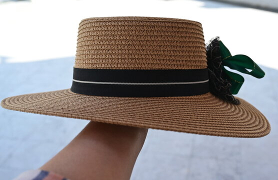 Left hand holds a sailor's straw hat with a green bow with black stripes on the side. Stylish image details for women's fashion Used for wearing to protect from heat and sunlight in nature.
