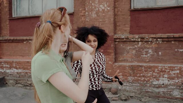 Three young multiethnic girl friends hugging and dancing while walking. Young group of friends actively chatting at the streets of old town. Hipsters in the old city. High quality 4k footage