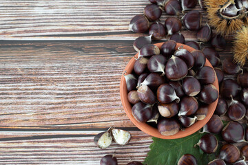 Brown chestnuts in a bowl on wooden background. Copy space. Top table view. Natural sweet autumn fruit harvest.