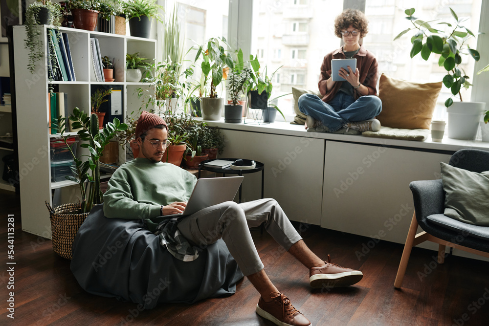 Aufkleber young woman with tablet sitting on windowsill in front of male colleague with laptop networking in a