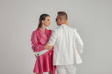 Stylish confident young couple in elegant fashionable clothes posing on grey isolated background, hugging and posing. Studio shot of show presenter, dancer, model ad concept. Copy text space