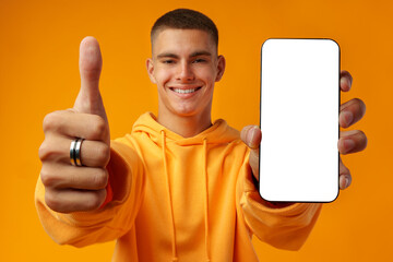 Smiling young man showing mobile phone blank white screen on yellow background