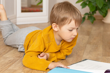 Naklejka premium A little boy is reading sitting on the floor.