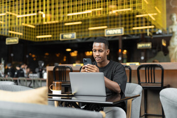 Portrait of handsome young African man using laptop computer in coffee shop - 544114650