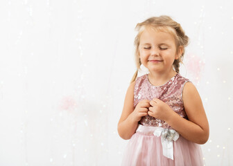 Сute young blonde girl in a pink sparkly fancy dress is standing and smiling.