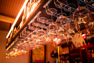 Empty upside-down crystal wine glasses hanging on the bar top counter in luxury restaurant. Nightlife dinner atmosphere and glassware concept