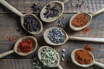 Set of spices in wooden spoons, closeup, top view. Various pepper, chili peppers, cardamom, carnation, star anise, paprika, and saffron for cooking