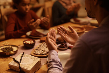 Close up of Muslim man praying with his family at dining table.