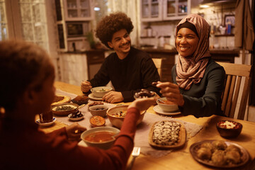 Happy black Muslim woman eating with her family at dining table.