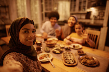 Happy Muslim woman taking selfie with her family at dining table.