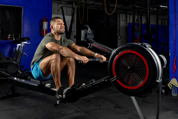 Fototapeta na wymiar Side view of a Latin man with sportswear, rowing on a machine in a crossfit gym
