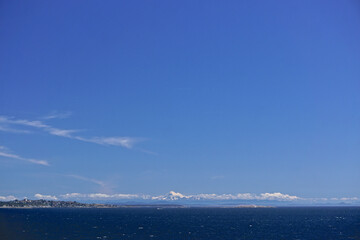 Morning at sea: Clouds and fog over Alaskan islands in the North Pacific Ocean with snow-capped mountains in the distance.