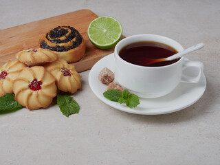 mint tea in a white cup with cookies and lemon on white marble, flat plate