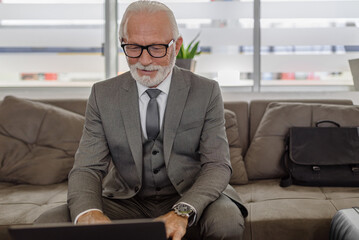 Confident entrepreneur using laptop while sitting on sofa at the corporate office.